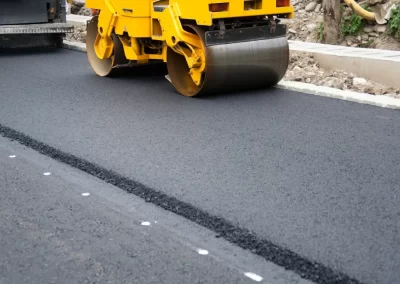 A yellow steamroller from Action Paving smooths fresh asphalt on a newly paved road near a curb, showcasing professional asphalt paving solutions.