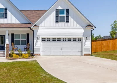 White suburban house in Middletown NY with a two-car garage, driveway expertly finished by Asphalt Paving Experts, lush lawn, and wooden fence under a clear blue sky.
