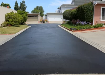 Freshly paved black asphalt driveway by Action Paving in Middletown NY, leading to garages and bordered by green lawns and houses under a blue sky.