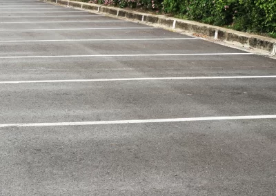 Empty parking lot with marked spaces and greenery in Middletown NY, featuring a partially visible white car behind bushes—expertly finished by Action Paving, your local asphalt paving experts.