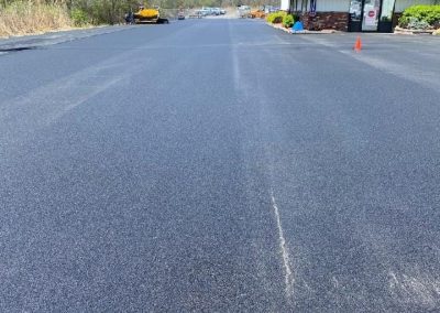 A freshly paved asphalt parking lot beside a building, completed by Asphalt Paving Experts in Middletown NY, with some vehicles and trees in the background.
