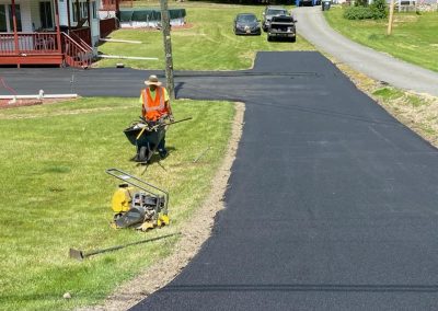 A worker in an orange vest stands by fresh asphalt from Action Paving, showcasing quality asphalt paving solutions on a sunny residential street in Middletown NY.