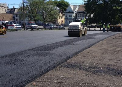 Asphalt Paving Experts use a steamroller to pave fresh asphalt on a parking lot under a clear blue sky in Middletown NY.