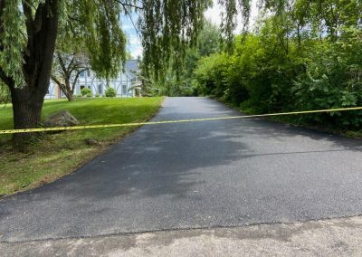 A driveway blocked by yellow caution tape, with trees and a house in the background, hints at fresh asphalt paving solutions underway in Middletown NY.