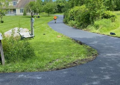 A paved path curves through greenery in Middletown NY; a person in an orange shirt walks away in the distance, showcasing quality asphalt paving.